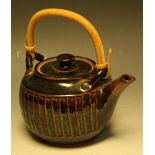 A salt glazed stoneware teapot, by Geoffrey Whiting, in shades of black and brown, cane handle,