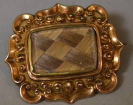 A Victorian mourning brooch, with central plait of hair work panel, shaped yellow metal frame,