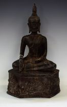 A Tibetan bronze Buddha, modelled seated above a mask head cushion,