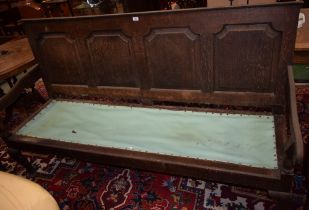 An 18th century oak settle, four fielded panels to back, open arms, cabriole forelegs, pad feet,