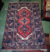 A Persian woollen rug, with three geometrical motifs, banded geometrical borders, in red,