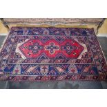 A Persian woollen rug, with three geometrical motifs, banded geometrical borders, in red,