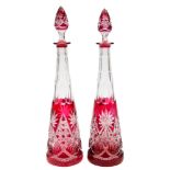 A pair of ruby overlaid clear glass decanters and stoppers: of slender tapering form with star and