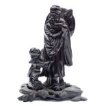 A Chinese black composition carved figure: of a beaded man with a shield and sword on his back,