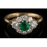 An emerald and diamond cluster ring: the central round emerald approximately 4.5mm diameter x 3.