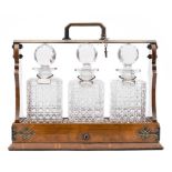 An Edwardian oak three decanter tantalus: the oak and silver plated frame with hinged fall front