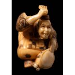 A Japanese carved ivory netsuke depicting a musician: beating a drum with his fan,