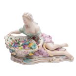 A Meissen figural sweetmeat dish: the shaped bowl applied with flowers and supported by a reclining