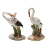 Two Meissen miniature models of storks: one holding a swaddled baby in its beak,