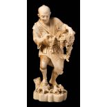 A Japanese carved ivory okimono of a grape gatherer: in traditional costume holding a basket of