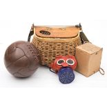 A wicker creel together with a brown leather football and a WWII childs gas mask.