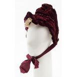 A late Victorian purple velvet bonnet, with lace trim and ribbon ties.