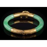 An early 20th century Chinese gold mounted green jade hinged bangle: with two hinged sections of