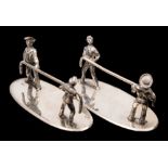 A pair of Edwardian silver plated knife rests of an army and navy tug o'war:,