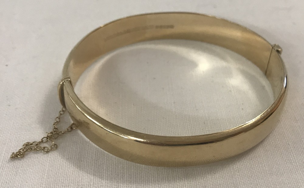 A 9ct gold hinged bangle with safety chain.