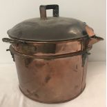 A large antique copper lidded pot with handles, pouring spout and riveted bars on side.