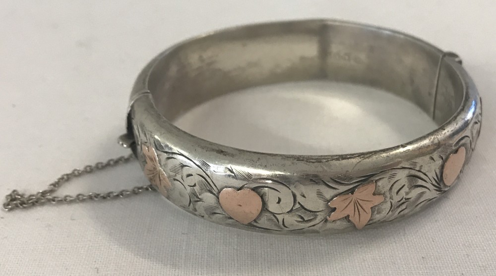 A silver hinged bangle with gold heart and ivy leaf decoration, complete with safety chain.