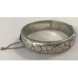 A silver hinged bangle with gold heart and ivy leaf decoration, complete with safety chain.