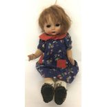 A vintage composition walking doll with painted face and closed mouth in blue floral dress.