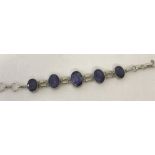 A 925 silver bracelet set with 5 oval cut purple charoite stones in graduating sizes.
