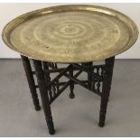 An oriental brass table on a hexagonal wooden folding stand.