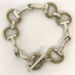 A silver and gold tone metal decorative stirrup link bracelet with T bar fixing.