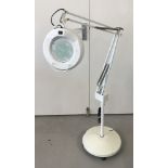 A large white, floor-standing angle poise magnifier light on castors.