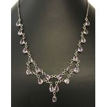A dress necklace set with 31 teardrop cut amethysts in silver surrounds on a silver belcher chain.