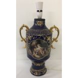 A blue ceramic 2 handled vase/urn, heavily gilded with classical panel design to front and back.