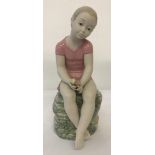 A large Nao ceramic figurine of a girl sitting on a rock, wearing a pink dress and holding flowers.