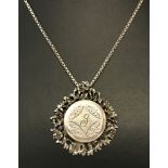 A vintage silver locket with central engraved letter J, mounted in a decorative surround.