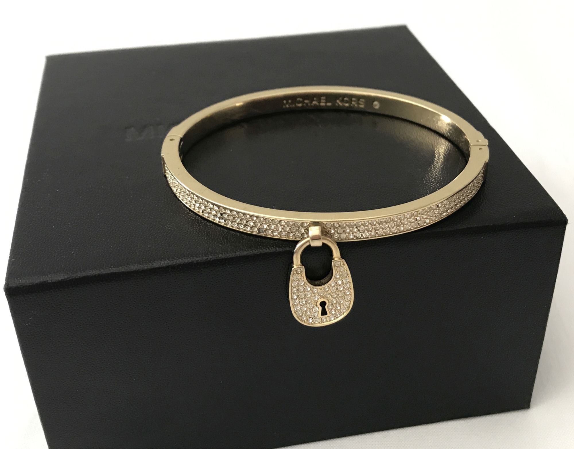 A Michael Kors gold tone hinged pave set bangle with padlock charm.