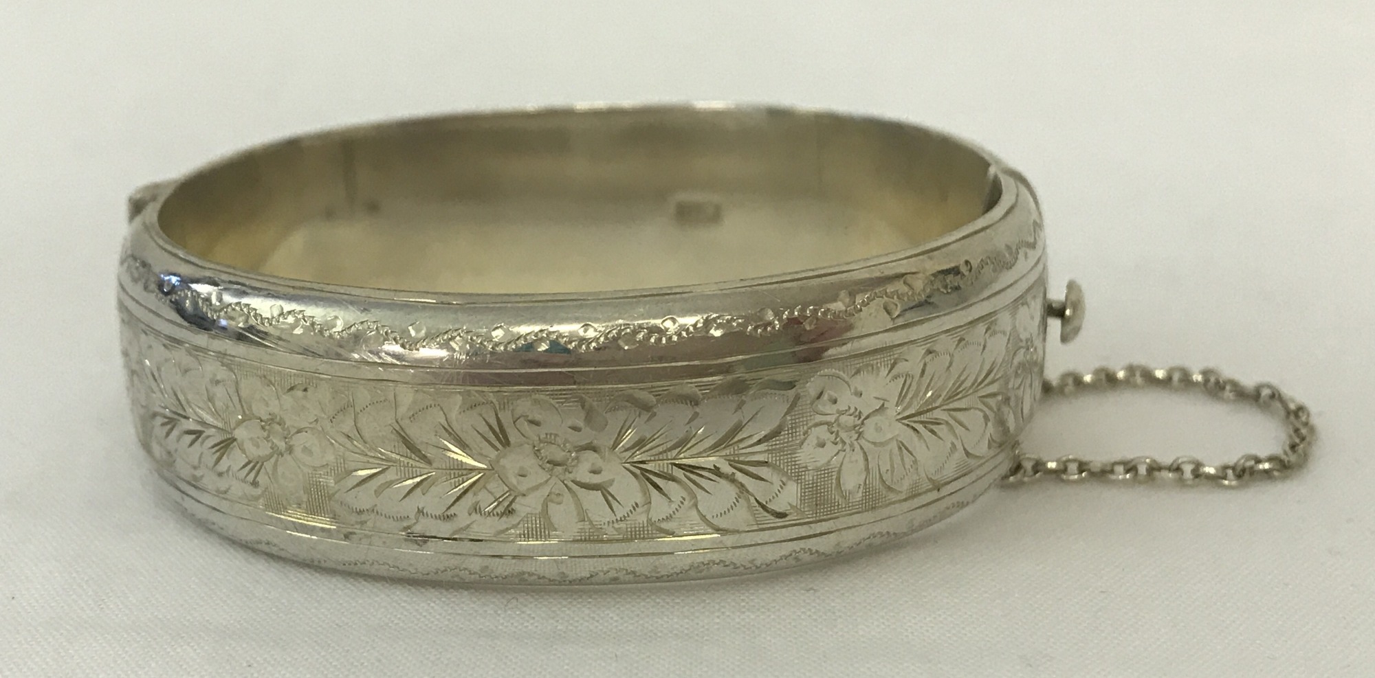 A vintage half engraved silver bangle with floral decoration, complete with safety chain.