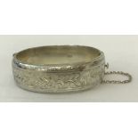 A vintage half engraved silver bangle with floral decoration, complete with safety chain.