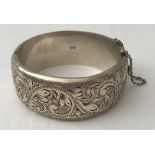 A vintage silver bangle with floral engraved detail and safety chain.