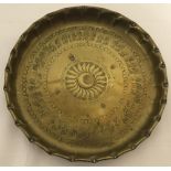A brass circular dish with hammered Persian decoration to interior and shaped rim.