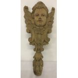 A carved wooden cherub wall hanging with small ceramic eyes.