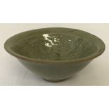 A small round celadon glazed bowl with oriental figure, flower and leaf detail to inner bowl.