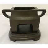 A square shaped Chinese, 2 handled, bronze censer on a pedestal stand.