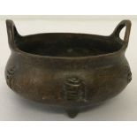 A small bronze 2 handled censer, raised on tripod feet & with calligraphy detail to outer bowl.