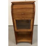 A small light wood cabinet with tambour shutter, pull down cupboard door and open lower shelf.