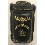 A black cast iron wall hanging letter box with detail painted in gold.