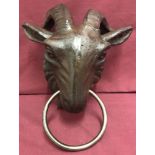 A cast iron door knocker of a goats head holding a ring in its mouth.