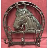 A cast iron wall hanging horseshoe plaque with 3 folding coat hooks.