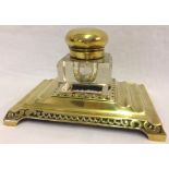 A Victorian brass four footed desk stand with central heavy glass, brass lidded inkwell.