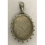 An antique large white metal locket with bead style detail to edges and floral engraving to front.