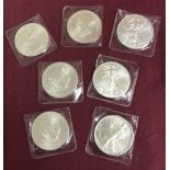 7 uncirculated American silver dollars in clear plastic cases.