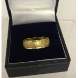 An 18ct gold decorative wedding band. Brushed design to centre with cut detail to edges.