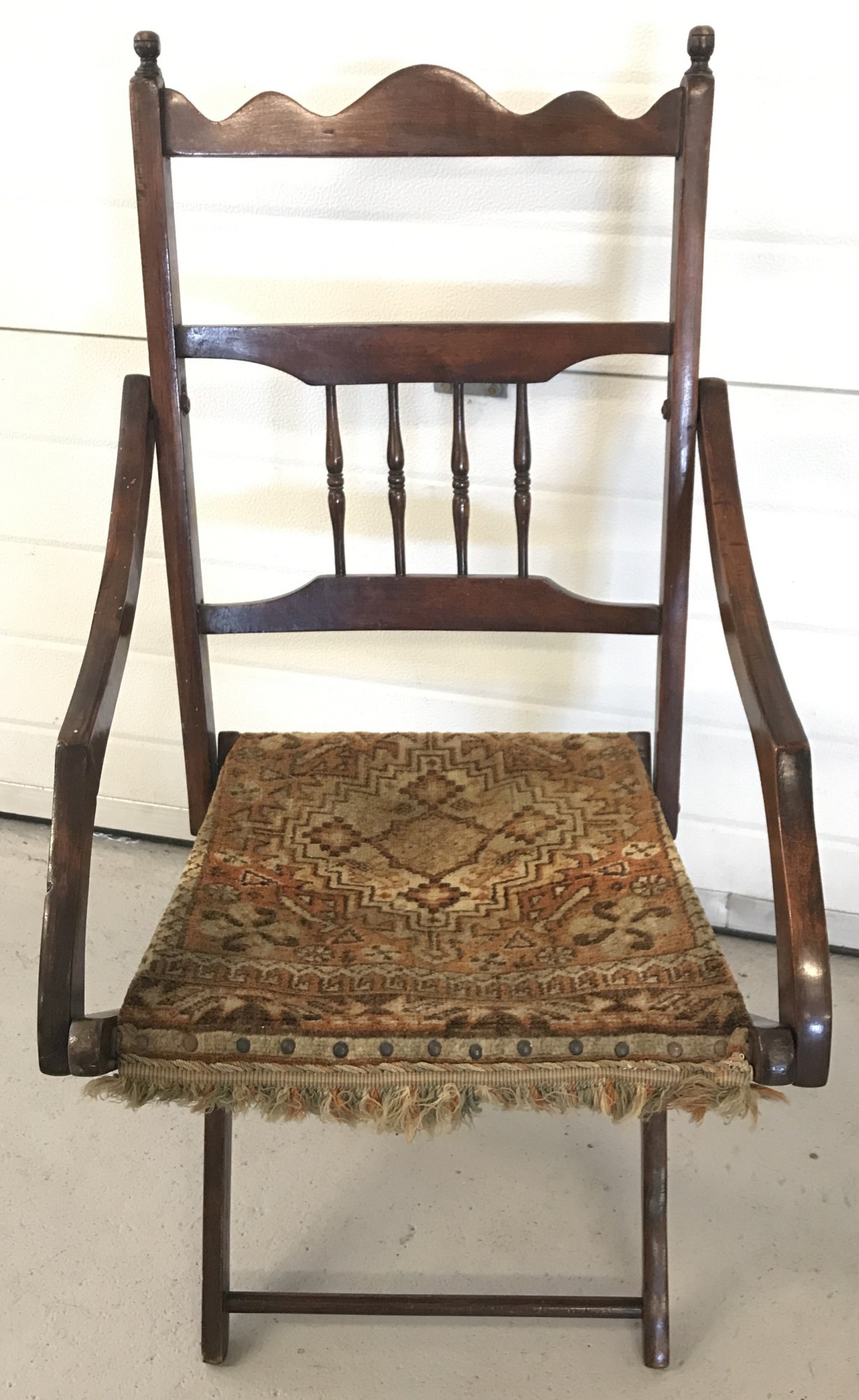 A vintage folding dark wood chair with carpet seat and spindle decoration to back.