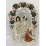 A large Staffordshire ceramic figurine of a courting couple sat beneath a bough of grape vines.
